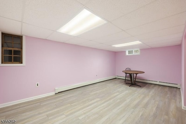below grade area featuring light wood-style floors, a paneled ceiling, baseboards, and baseboard heating