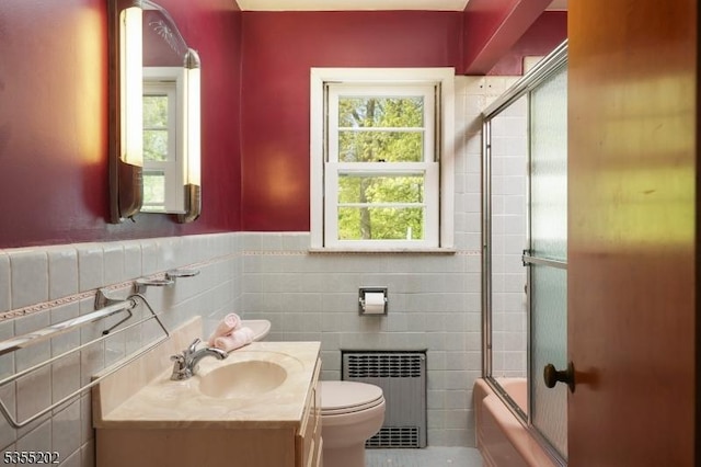 bathroom with tile walls, bath / shower combo with glass door, vanity, toilet, and radiator