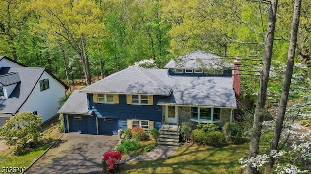 split level home featuring a chimney, an attached garage, driveway, and a forest view