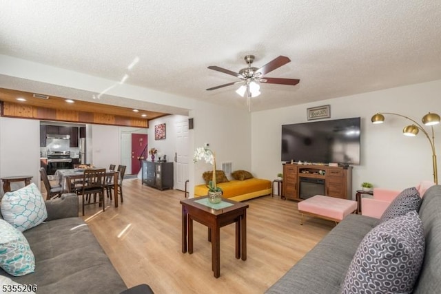 living room with visible vents, a textured ceiling, light wood finished floors, and a ceiling fan