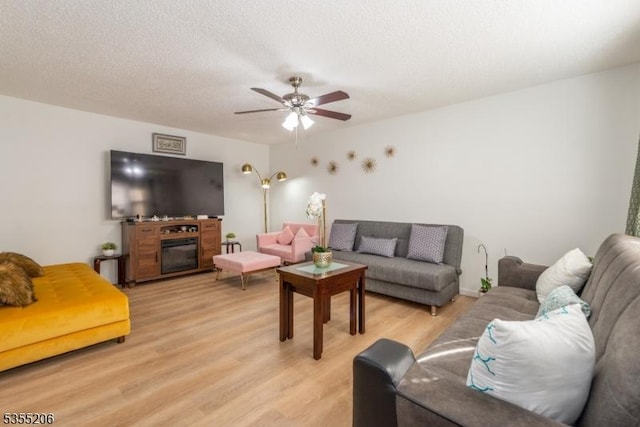 living room with ceiling fan, a glass covered fireplace, and light wood finished floors