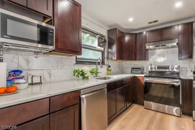 kitchen with visible vents, a sink, light countertops, under cabinet range hood, and stainless steel appliances