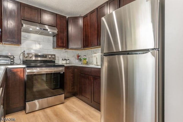 kitchen featuring decorative backsplash, a toaster, under cabinet range hood, light wood finished floors, and appliances with stainless steel finishes