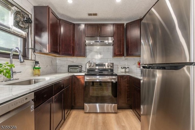 kitchen with ventilation hood, a sink, light wood-style flooring, appliances with stainless steel finishes, and backsplash