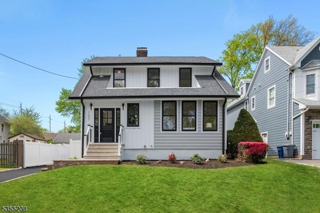 view of front of property with fence, roof with shingles, board and batten siding, a front yard, and a chimney