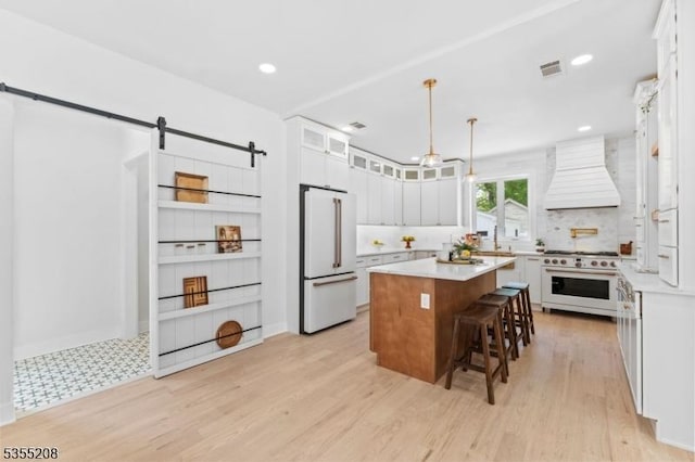 kitchen featuring a barn door, a breakfast bar area, premium appliances, visible vents, and custom exhaust hood
