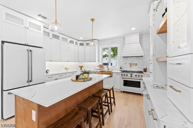 kitchen with visible vents, custom exhaust hood, glass insert cabinets, high quality appliances, and white cabinetry
