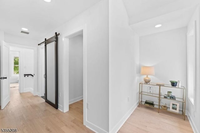 corridor with visible vents, light wood-style floors, baseboards, recessed lighting, and a barn door