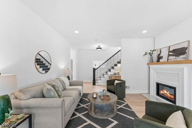 living area with stairs, recessed lighting, a glass covered fireplace, and wood finished floors