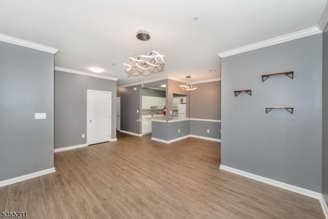 unfurnished living room with a chandelier, ornamental molding, wood finished floors, and baseboards