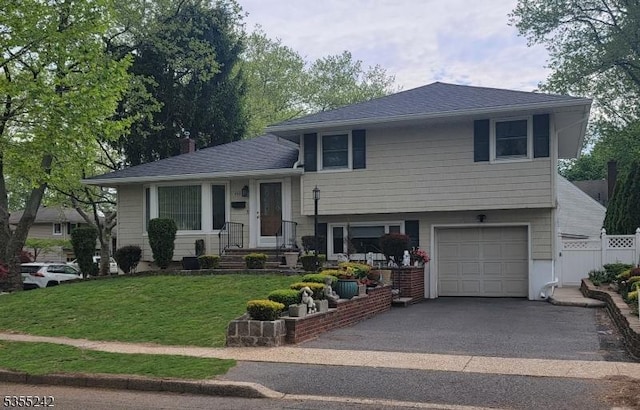 split level home with fence, roof with shingles, an attached garage, a front lawn, and aphalt driveway