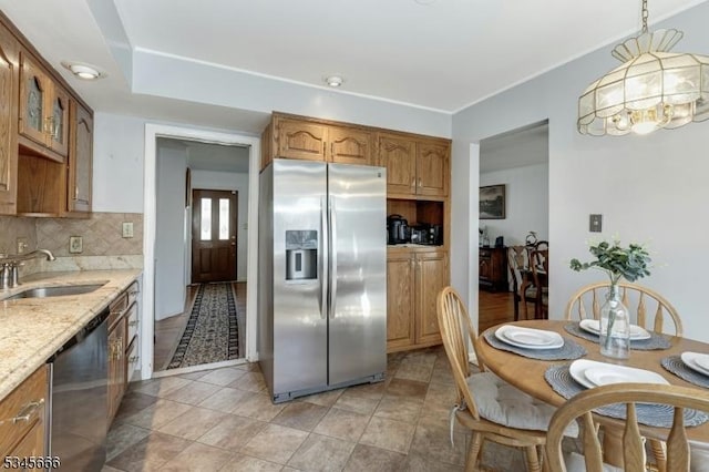 kitchen featuring brown cabinets, light stone counters, a sink, stainless steel appliances, and tasteful backsplash