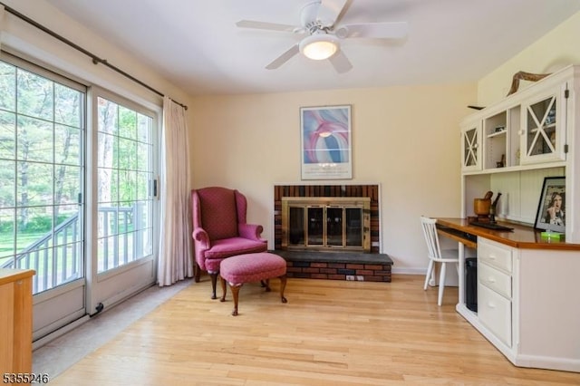 sitting room with a brick fireplace, a ceiling fan, and light wood-style floors