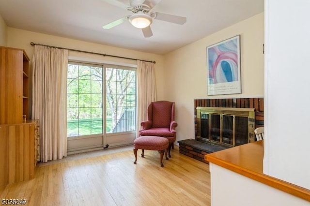 living area with light wood-type flooring, a ceiling fan, and a fireplace