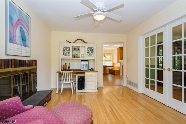 living room with ceiling fan, light wood-style floors, a glass covered fireplace, french doors, and visible vents