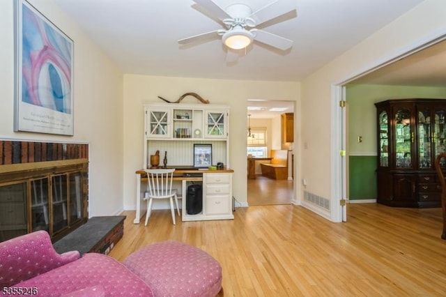 living area with ceiling fan, visible vents, baseboards, a glass covered fireplace, and light wood-style flooring