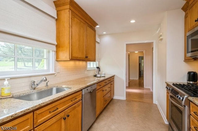kitchen featuring decorative backsplash, light stone countertops, brown cabinets, a sink, and stainless steel appliances
