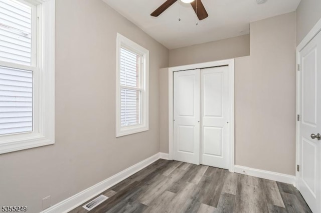 unfurnished bedroom with a ceiling fan, baseboards, wood finished floors, visible vents, and a closet