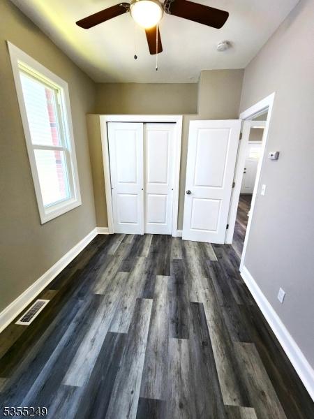 unfurnished bedroom with baseboards, a ceiling fan, dark wood finished floors, and a closet