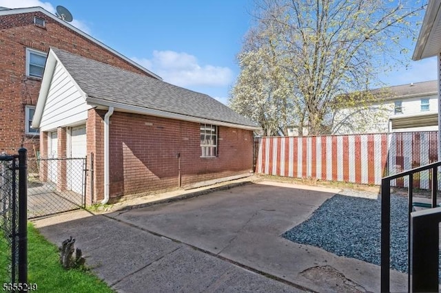 view of side of home with brick siding, a garage, fence, and a shingled roof