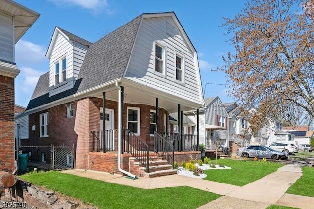 view of front of house featuring a front yard, a gambrel roof, roof with shingles, brick siding, and a porch