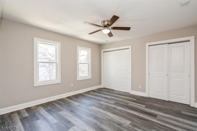 unfurnished bedroom featuring dark wood-style flooring, baseboards, multiple closets, and ceiling fan