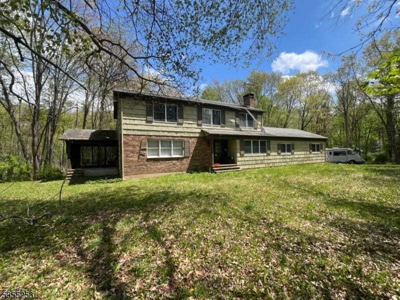 back of property with a lawn, brick siding, a chimney, and a sunroom