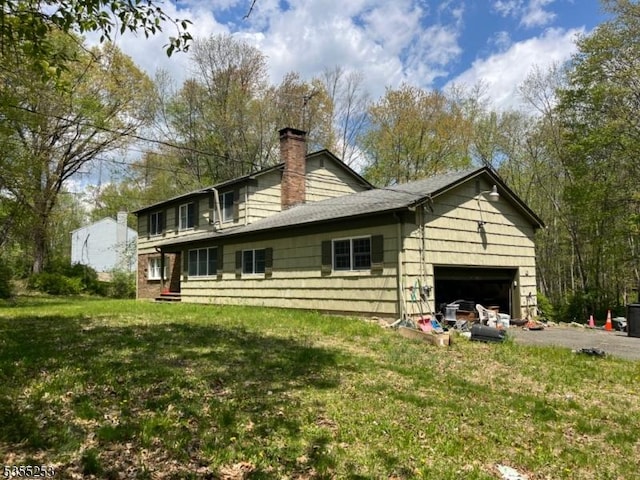 back of property featuring a yard, an attached garage, driveway, and a chimney