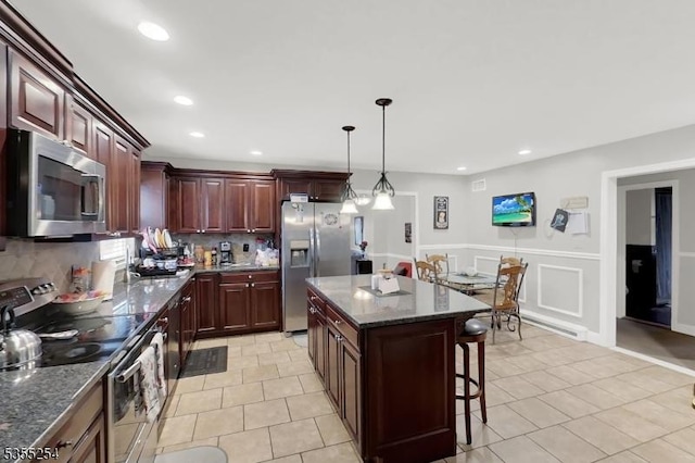 kitchen with appliances with stainless steel finishes, tasteful backsplash, a kitchen bar, light tile patterned floors, and a kitchen island