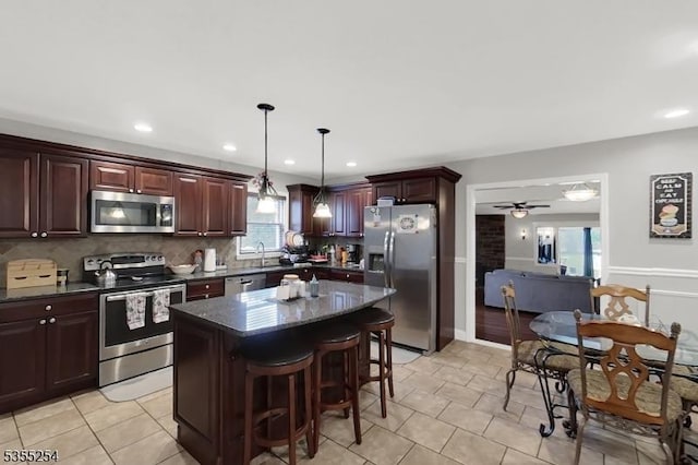 kitchen with appliances with stainless steel finishes, backsplash, a kitchen bar, a center island, and ceiling fan