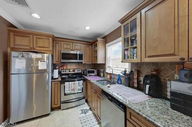 kitchen featuring stainless steel appliances, a sink, crown molding, light stone countertops, and glass insert cabinets