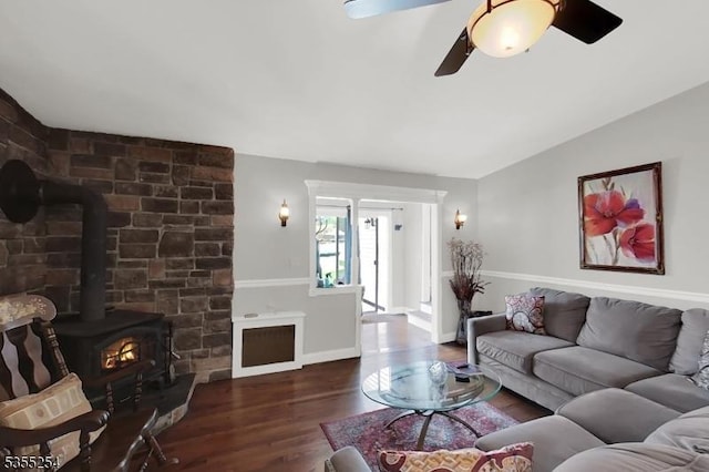 living room featuring a wood stove, ceiling fan, wood finished floors, vaulted ceiling, and baseboards