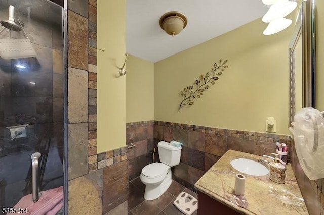 full bath featuring tile walls, wainscoting, tiled shower, toilet, and vanity