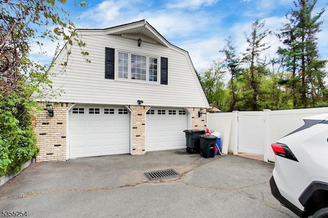 view of side of property with brick siding, asphalt driveway, a gambrel roof, fence, and a garage
