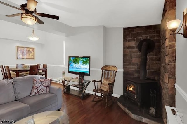 living room with a wood stove, wood finished floors, ceiling fan, and baseboards