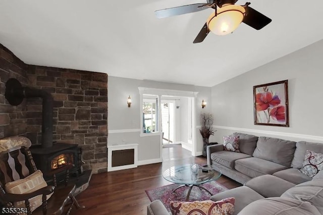 living area featuring a wood stove, wood finished floors, vaulted ceiling, baseboards, and a ceiling fan