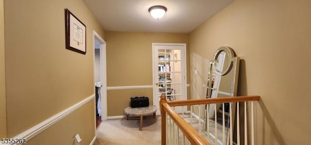 hall featuring carpet floors, baseboards, and an upstairs landing