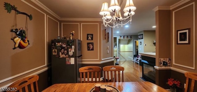 dining area with ornamental molding, a decorative wall, wood finished floors, and a notable chandelier