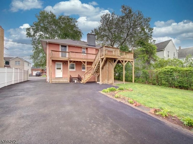 back of property with stucco siding, a chimney, a wooden deck, stairway, and a yard