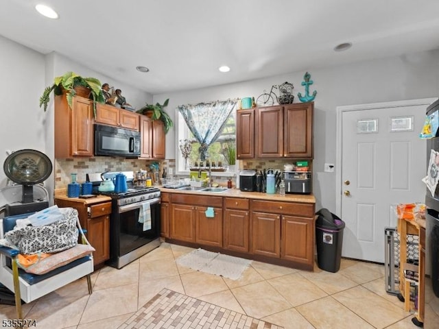 kitchen featuring stainless steel range with gas cooktop, black microwave, decorative backsplash, and a sink