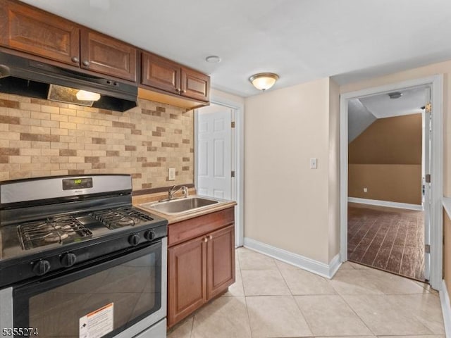 kitchen with a sink, gas range, baseboards, tasteful backsplash, and under cabinet range hood