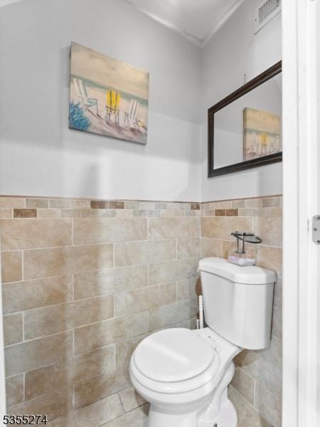 bathroom with toilet, tile patterned floors, a wainscoted wall, tile walls, and visible vents