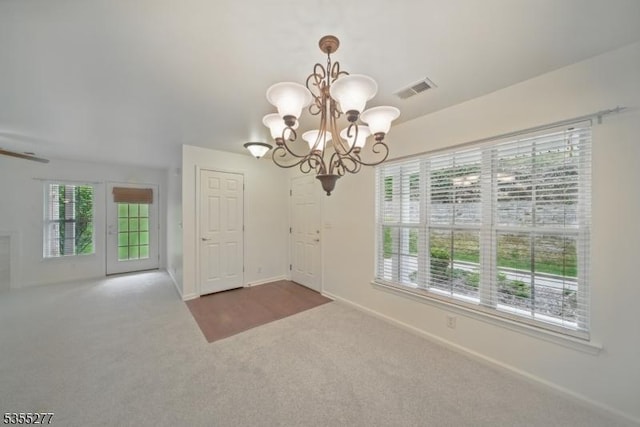 unfurnished dining area with an inviting chandelier, carpet floors, baseboards, and visible vents