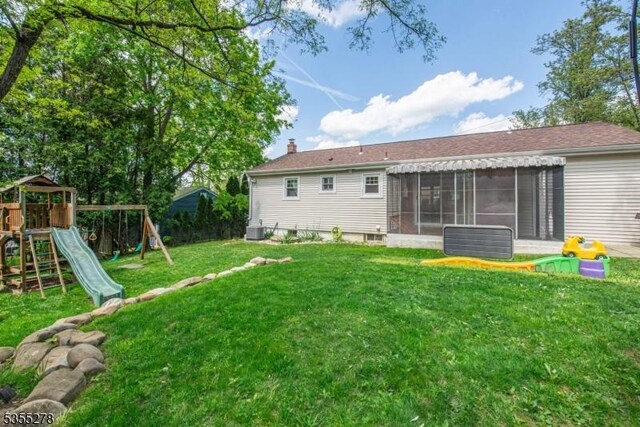 rear view of house featuring a sunroom, a playground, a lawn, central AC, and a chimney