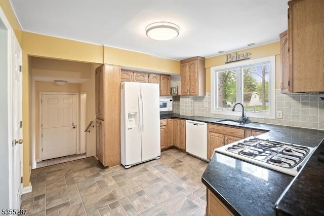 kitchen with white appliances, dark countertops, a sink, and decorative backsplash