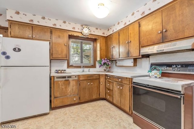 kitchen with brown cabinetry, a sink, wallpapered walls, under cabinet range hood, and white appliances