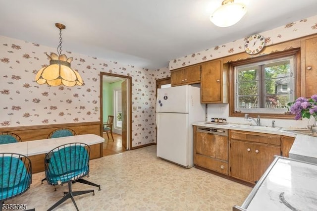kitchen with light countertops, freestanding refrigerator, wallpapered walls, and brown cabinetry