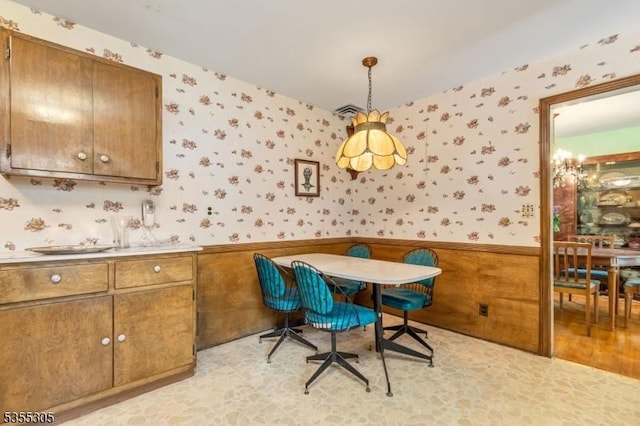 dining space with wallpapered walls, a notable chandelier, and a wainscoted wall