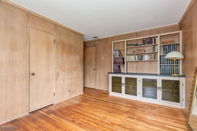 interior space with visible vents, crown molding, wood finished floors, and wooden walls