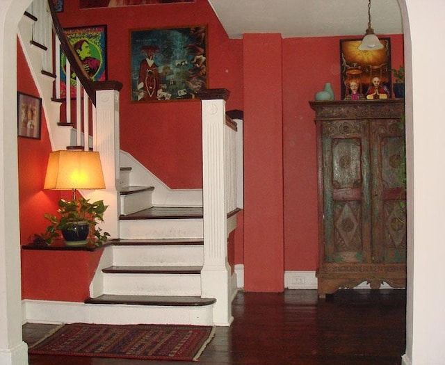 stairway featuring arched walkways, baseboards, and wood finished floors
